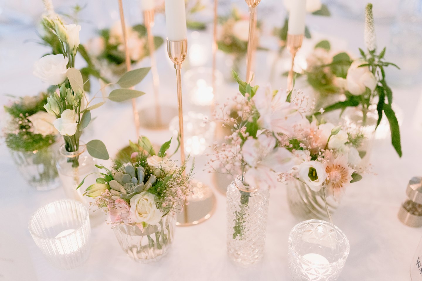 Elegant blomsterarrangemang med vita rosor och ljus på ett bord.