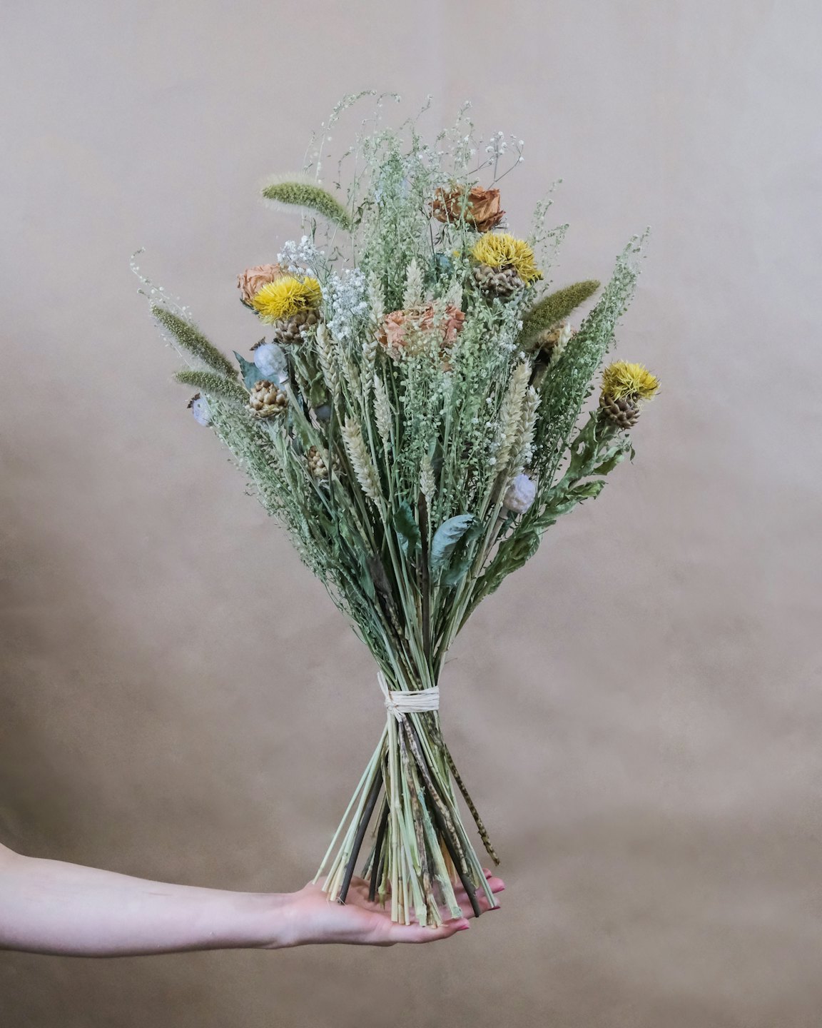 Hand håller en rustik bukett med torkade blommor och vete.