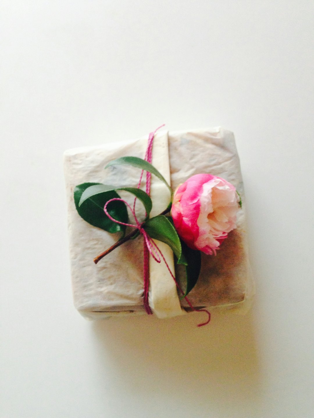 Presentförpackning inslagen i krulligt papper med en magentaröd rosett och kameliablomma.