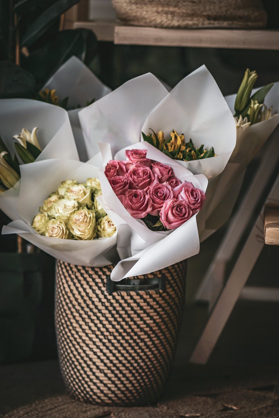 Vita blomsterbuketter i vitt papper står i en flätad korg.